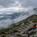 雲のかかる北海道の山並みと登山道に置かれたオレンジ色のザックのイメージ