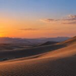 夕暮れの砂漠の砂丘に赤い旗が立つイメージ